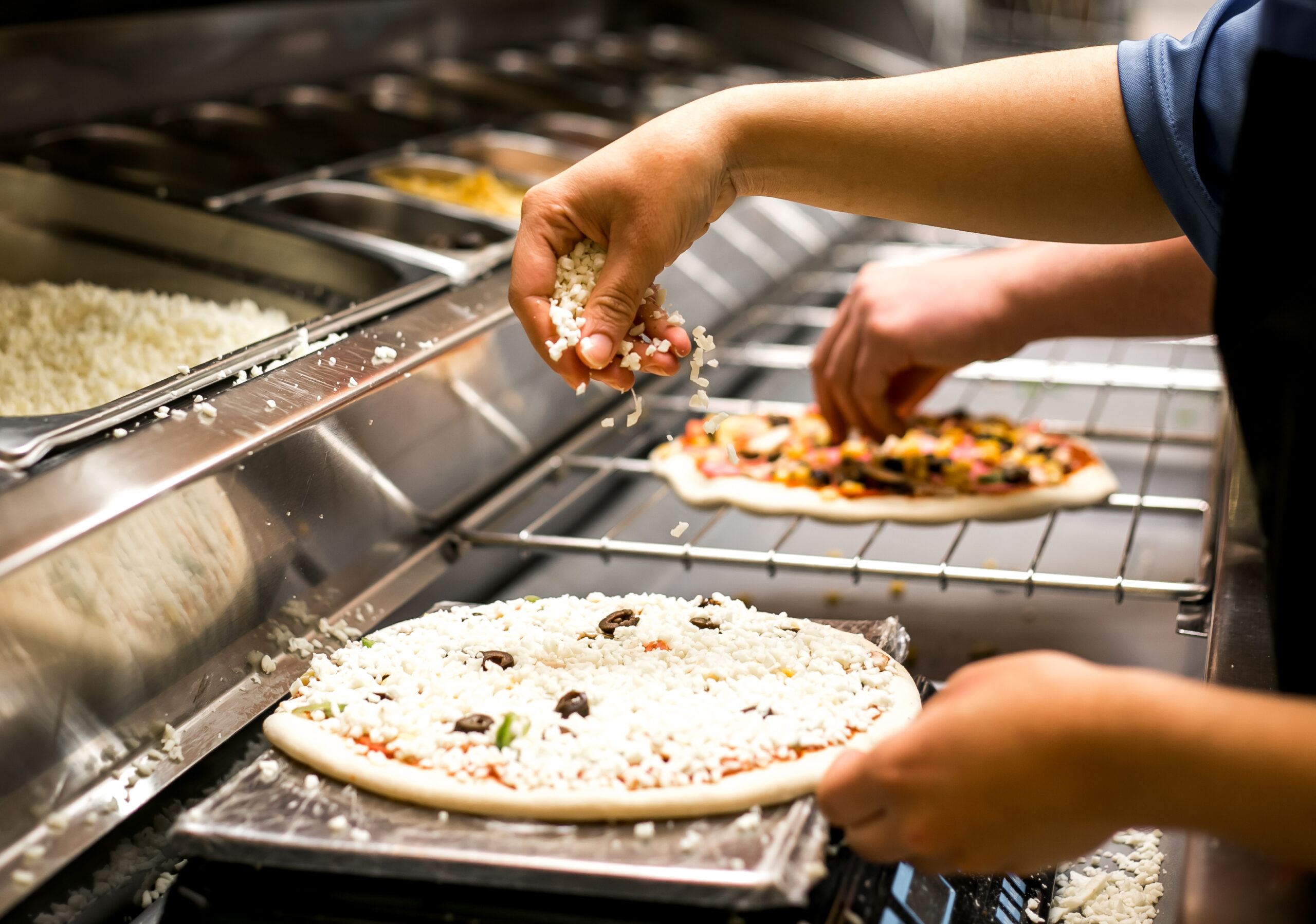 chef puts cheese on pizza dough covered with tomato sauce